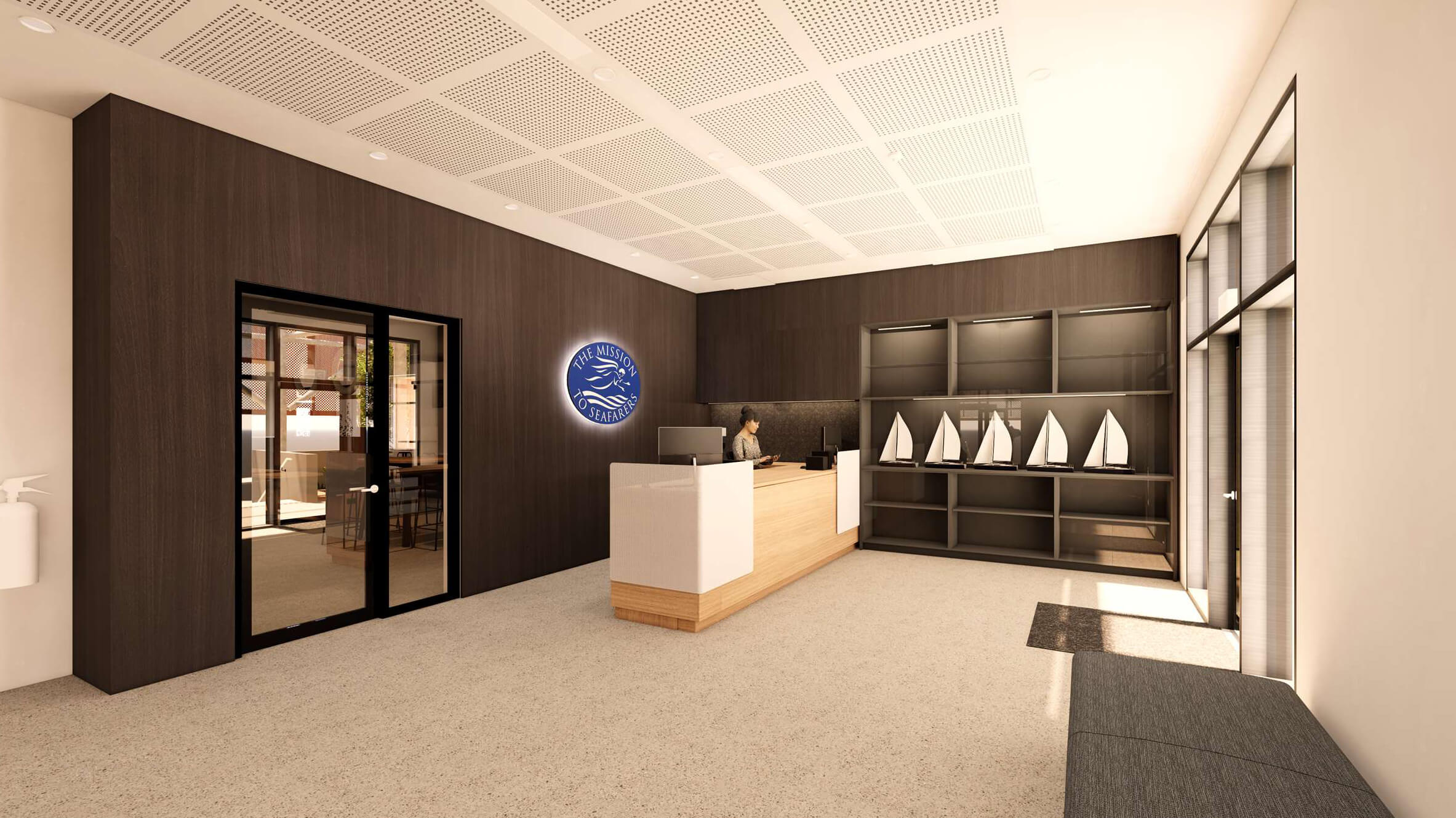 Modern lobby with wooden reception desk, a woman working behind it, and a wall display of six small sailboat models under a sign that reads The Mission to Seafarers.