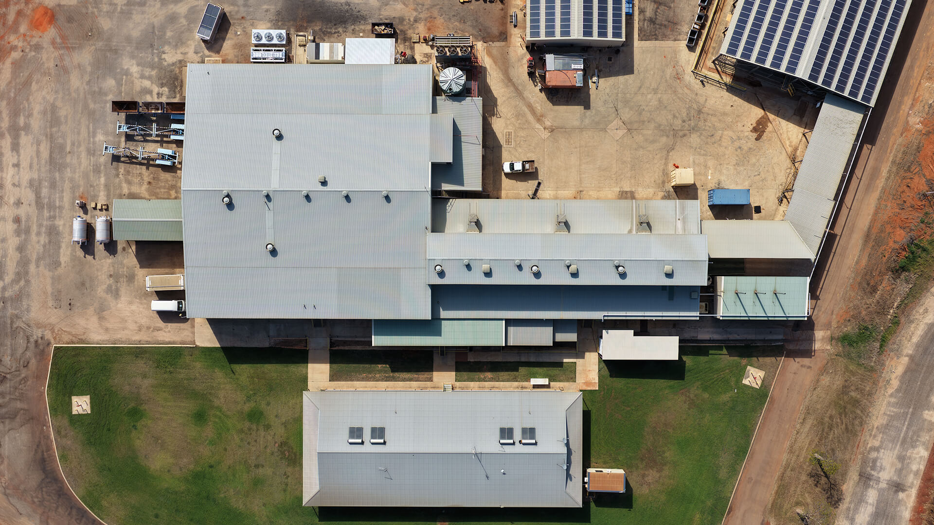 Aerial view of an industrial complex with multiple connected buildings and solar panels on one roof.