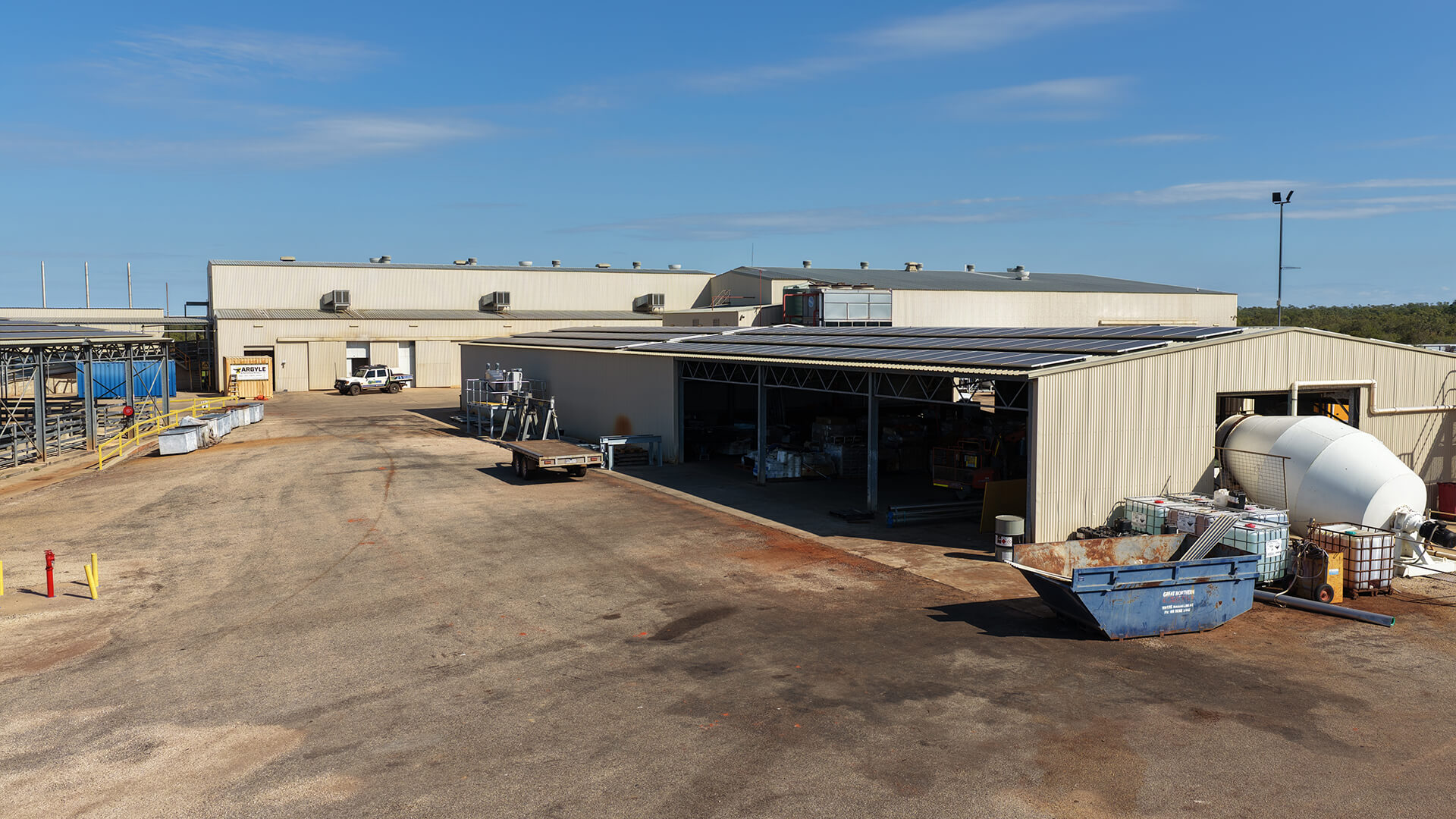 Industrial warehouse complex with large open yard, parked truck, and storage containers under clear sky.