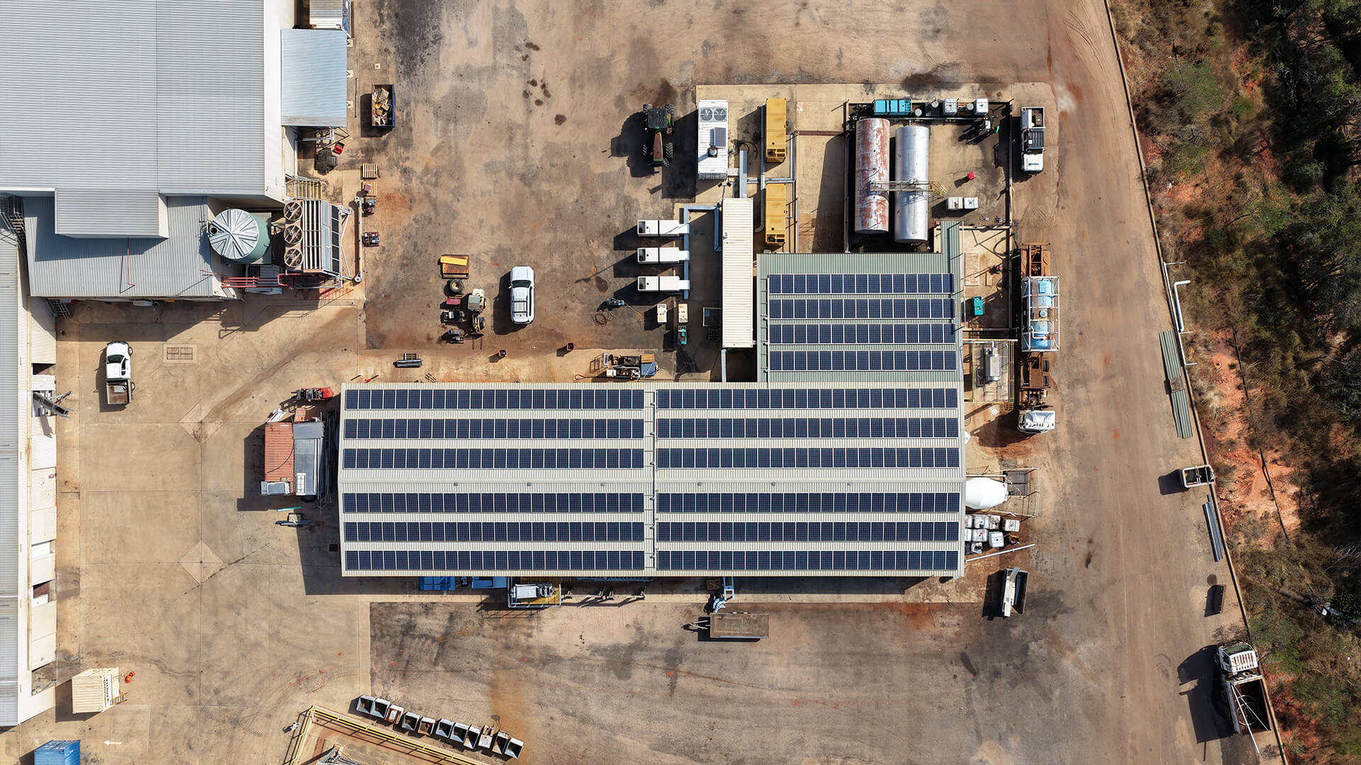 Aerial view of an industrial facility with solar panels on the roof and vehicles on concrete ground.